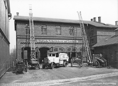 Foto: Ein Haus. Davor ein alter Feuerwehrwagen und zwei lange Leitern.Aufschrift auf dem Haus: 'Städtische Volksbücherei und Lesehalle'