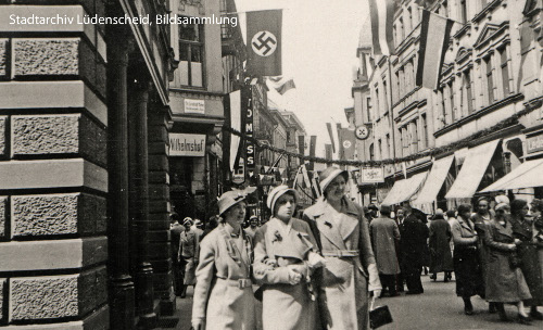 Foto: Blick in eine Strasse mit Hakenkreuzfahnen. Viele Menschen.