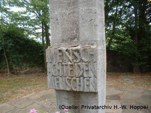 Foto: Eine Stele mit dem gemeißelten Schriftug 'MENSCH ACHTE DEN MENSCHEN'. Auf der Stele liegen kleine Steine.