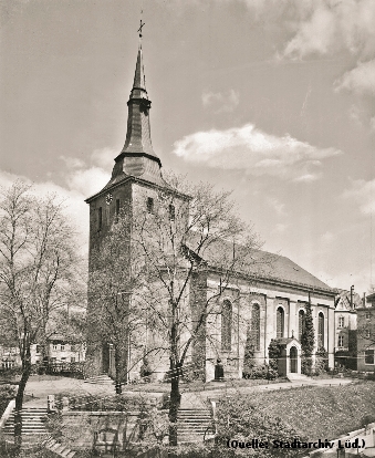 Foto: Das Foto zeigt eine Kirche. Davon eine Freitreppe die zum Eingang führt. Im Vordergrund Bäume.