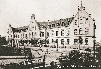 Foto: Ein breites Haus mit drei Giebelfassaden und Verzierungen daran. Davor eine Strasse.