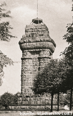 Foto: Ein Turmartiges Denkmal, auf welchem sich eine Feuerschale befindet. Bäume ringsum.