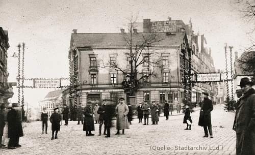 Foto: Zwei Strassen gabeln sich. An der Gabelung steht ein Haus: Eine Gastwirtschaft. Davor einige Männer.