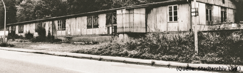 Foto: Eine lange Holzbaracke an einer Strasse.